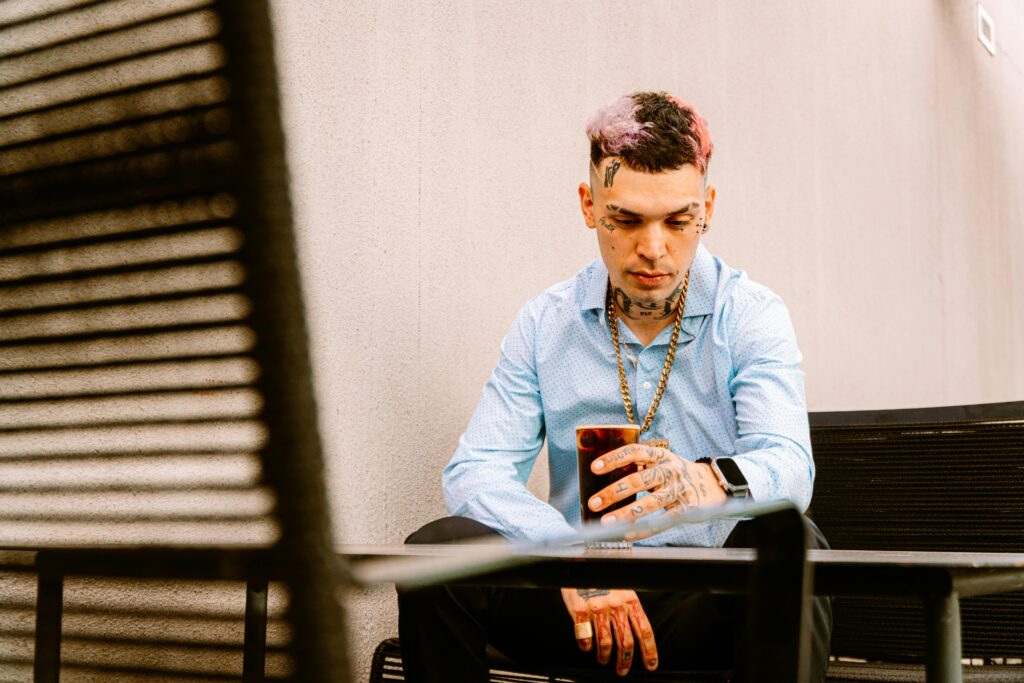 A tattooed man with a drink, sitting outdoors in Buenos Aires, showcasing modern fashion.
