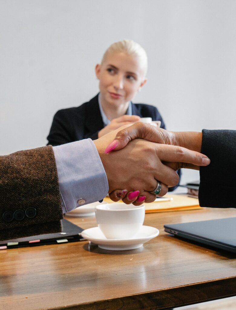 Crop faceless multiracial coworkers sitting at table and shaking hands after successful agreement in workspace